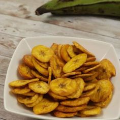 a white bowl filled with sliced bananas on top of a wooden table next to a banana plant