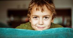 a young boy is peeking over the edge of a couch with his eyes wide open