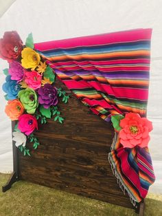 a wooden bench decorated with colorful flowers and ribbons on the top, in front of a white tent