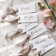 four pieces of paper with calligraphy on them next to some pink flowers and leaves