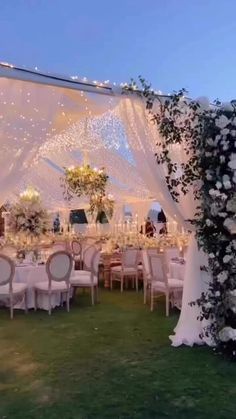 an outdoor wedding reception setup with white linens and greenery on the grass, surrounded by string lights