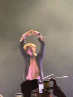 a man standing on top of a stage holding his hands up in the air with one hand above his head