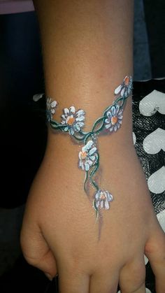 a woman's hand with white flowers painted on it and a green band around the wrist