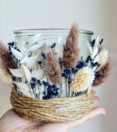 a hand holding a glass jar with dried flowers in it and twine wrapped around the top