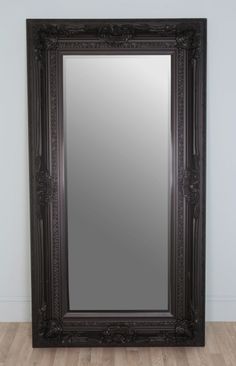 a large black framed mirror sitting on top of a wooden floor