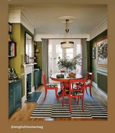 a dining room with green walls and white trim on the ceiling, red chairs around a round wooden table