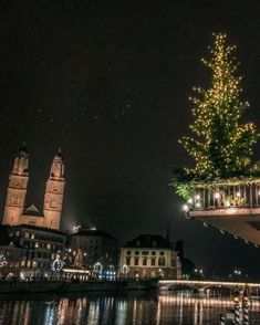 a large christmas tree is lit up in the night sky over a river and buildings