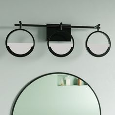 two circular mirrors are hanging on the wall above a round mirror and a black shelf