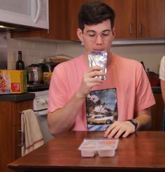 a man holding up a plastic container with food in it while sitting at a kitchen table