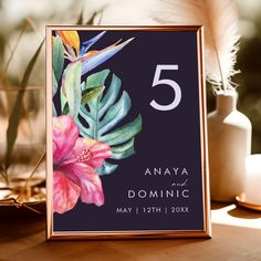 a wedding table number card with tropical flowers and leaves on the front in gold frame