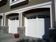 two white garage doors on the side of a house with stone wall and planter