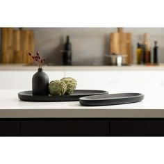 two black plates on a white countertop with some flowers in the vase and another plate next to it