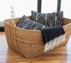 a basket that has some pillows in it on top of a wooden floor next to a window