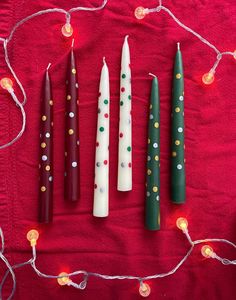 four candles are lined up on a red tablecloth with christmas lights in the background