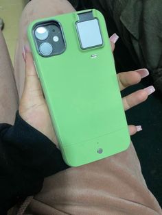 a person holding a green cell phone in their left hand and sitting on the ground