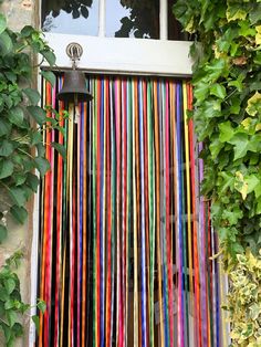 an open window covered in multicolored paper streamers next to a green bush