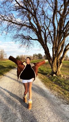 a woman walking down a dirt road next to a tree