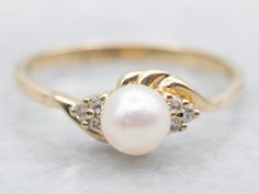 This ring is a stunning addition to any jewelry collection! Made of yellow gold, it features a lustrous pearl center flanked by brilliant diamond accents. Perfect for adding elegance and sophistication to any outfit. Metal: 14K Yellow Gold Gem: Pearl Gem Measurements: 5.1 mm, Round Accents: 6 Diamonds totaling .05 Carats, I in Clarity, G-H in Color Ring Size: 6.25 Marks: "S 14K" Stamped on the inside band SKU #: A42361 Each piece has been identified and graded by a Graduate Gemologist who has been certified by the Gemological Institute of America (GIA). We have six brick-and-mortar storefronts in Maine, Massachusetts, and New Hampshire and have been in business for over 25 years! Please visit our Shop's About Page or our website for more information about our jewelry. For questions about d Yellow Gold Rings With Diamond Accents And Pearl, Yellow Gold Pearl Ring With Center Stone, Yellow Gold Pearl Ring With Center Stone For Promise, Yellow Gold Pearl Diamond Ring With Accents, Pearl Ring Gold, Ring Pearl, Gold Pearl Ring, Pearl And Diamond Ring, Ring With Diamond