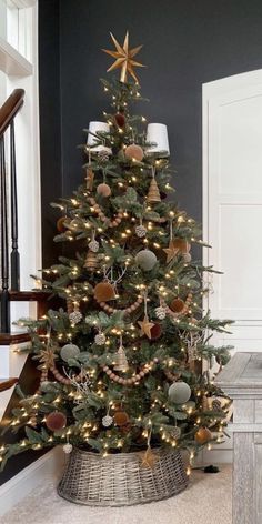 a small christmas tree with lights and ornaments in a basket on the floor next to stairs