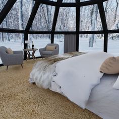 a bed sitting inside of a bedroom next to a window filled with snow covered trees