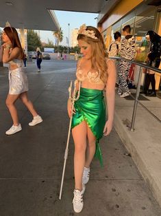 a woman in a green costume is walking down the street with a cane and headband