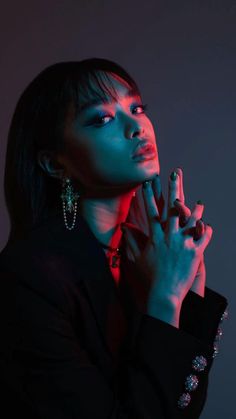 a woman in black shirt holding her hand up to her face with red light shining on her