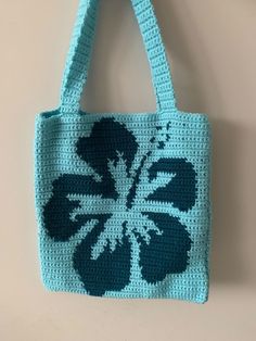 a crocheted bag hanging on a wall with a flower in blue and green