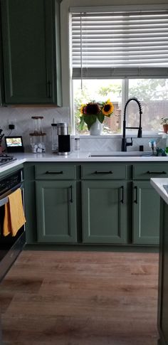 a kitchen with green cabinets and sunflowers on the window sill above the sink