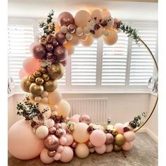 an arch made out of balloons and greenery is displayed in the corner of a room