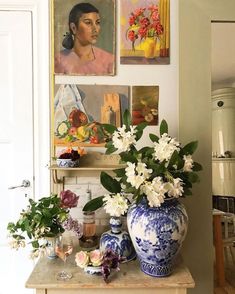 a table with vases and flowers on it in front of pictures hanging on the wall