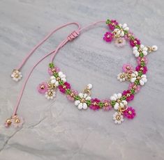 a pink bracelet with white and green beads on top of a marble table next to a pair of scissors