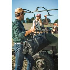 a man carrying a black bag while standing next to a woman on a golf cart