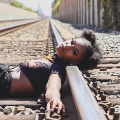 a woman laying down on train tracks with her arm around the rail road track and looking at the camera