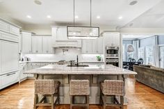 a large kitchen with white cabinets and wood flooring is pictured in this image, there are two chairs at the center island