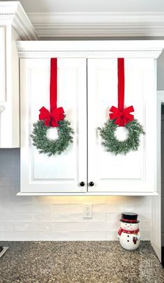 two wreaths are hanging on the cabinets in this kitchen decorated for christmas with red bows