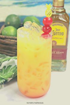 a pineapple margarita with a cherry garnish on the rim and a bottle of tequila in the background