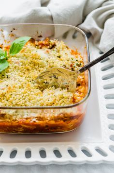 a casserole dish with cheese and vegetables in it on a white plate next to a fork