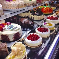 many different cakes are on display in a bakery case, including one with white frosting and the other with red raspberries