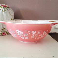 a pink bowl sitting on top of a white table next to a pillow and vase