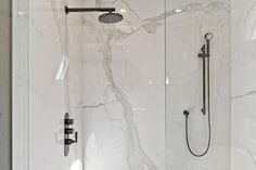 a walk in shower sitting next to a white tiled wall with black faucet