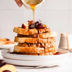 a stack of french toast with syrup being poured on top and grapes in the foreground