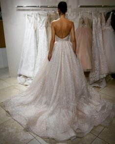 a woman in a wedding dress looking at dresses hanging on a rack with clothes behind her