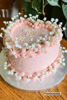 a pink heart shaped cake with white flowers on the top and bottom, sitting on a silver platter