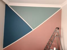 a ladder is in front of a wall painted with blue, pink and grey colors