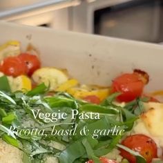 vegetable pasta in a white casserole dish with spinach, tomatoes and cheese