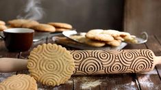 some cookies are sitting on a table next to a rolling pin and cup of coffee