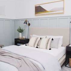 a bed with white linens and pillows in a small room next to a painting on the wall