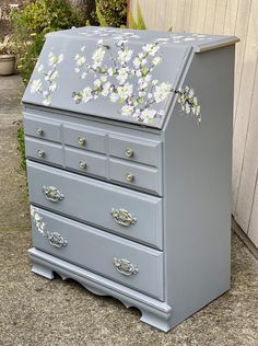 an old dresser with flowers painted on the top and bottom drawers is sitting in front of a house