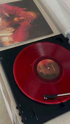 a red record player sitting on top of a table next to an album and vinyl