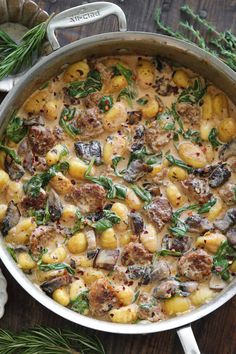 a pot filled with pasta and mushrooms on top of a wooden table next to herbs